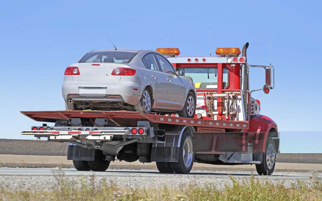 Car being towed on a flatbed truck illustrating why using AAA Plus roadside assistance is better than filing a towing claim with auto insurance.